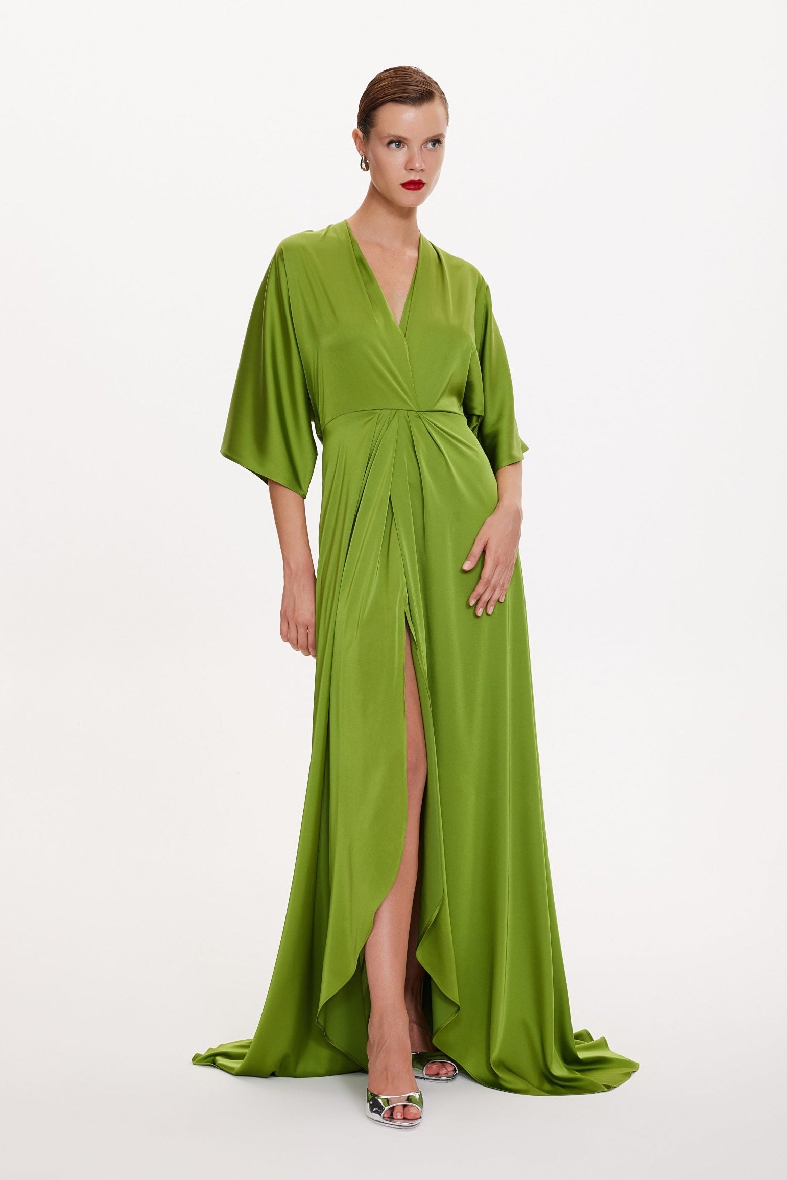 Woman wearing a green evening gown with a slit on a white background